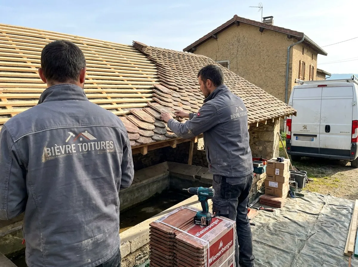 Deux couvreurs de Bièvre Toitures posent des tuiles écailles sur la toiture d'un lavoir près de La Côte-Saint-André